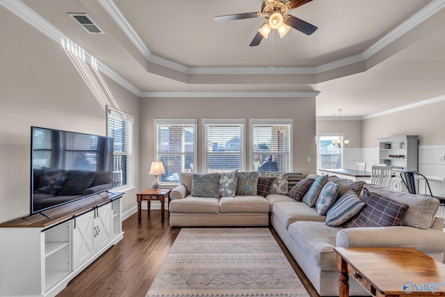 living room featuring crown molding, a tray ceiling, dark wood-type flooring, and plenty of natural light