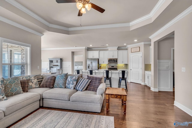 living room featuring a tray ceiling, dark wood-type flooring, ornamental molding, and ceiling fan