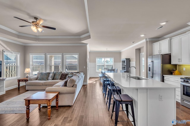 kitchen featuring sink, appliances with stainless steel finishes, white cabinetry, a center island with sink, and a kitchen bar