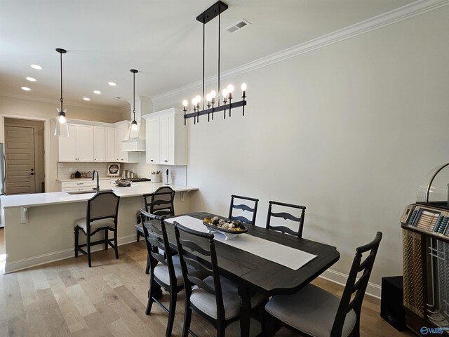 dining area featuring light wood-type flooring, ornamental molding, and a chandelier