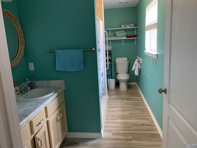 bathroom with baseboards, wood finished floors, vanity, toilet, and curtained shower