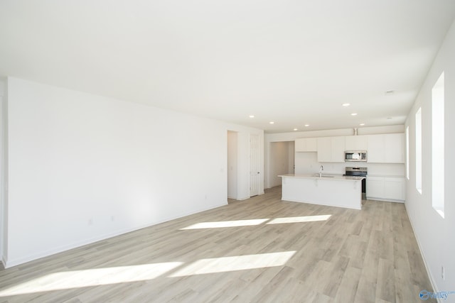 kitchen with light wood-type flooring, stainless steel appliances, white cabinets, sink, and a kitchen island with sink