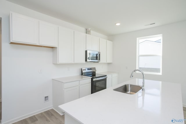 kitchen with sink, appliances with stainless steel finishes, white cabinets, and light hardwood / wood-style floors