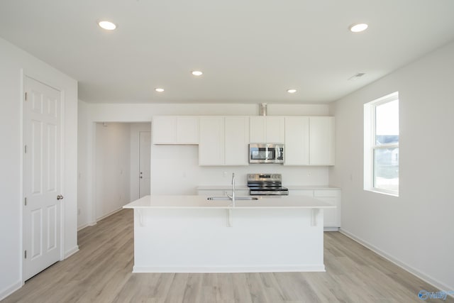 kitchen with sink, stainless steel appliances, white cabinetry, and an island with sink