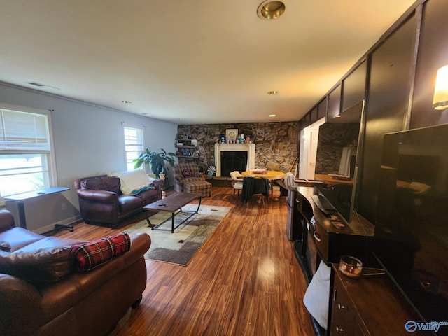 living room featuring dark wood-style flooring, a stone fireplace, and visible vents