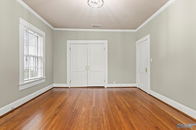 unfurnished bedroom with multiple windows, a closet, ornamental molding, and hardwood / wood-style flooring