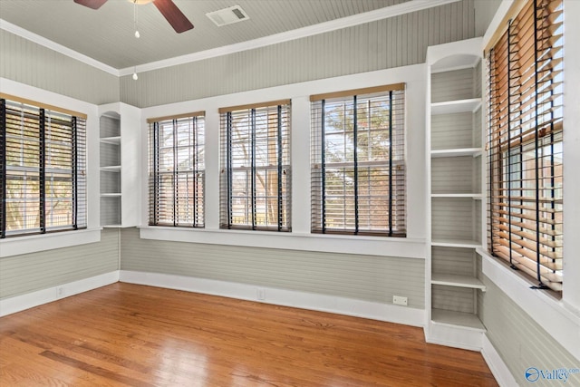 empty room featuring ceiling fan, built in features, wood-type flooring, and ornamental molding