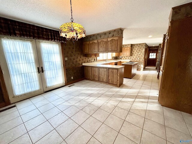 kitchen with a wealth of natural light, light countertops, a textured ceiling, a peninsula, and wallpapered walls