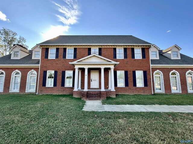 view of front of property with a shingled roof, a front yard, and brick siding