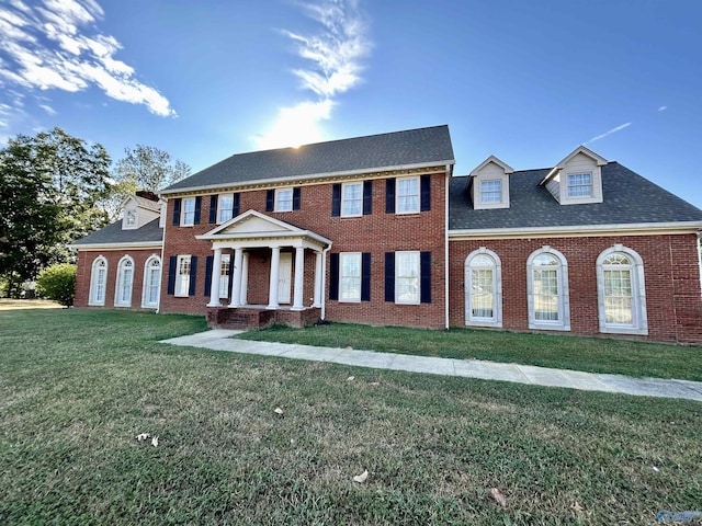 view of front facade featuring brick siding, a front yard, and a shingled roof