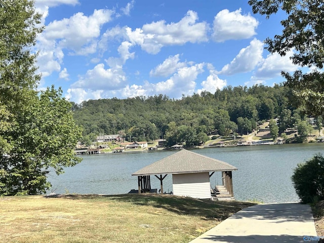 view of dock with a water view, a lawn, and a wooded view