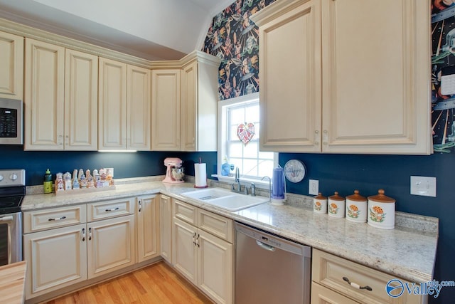 kitchen with light stone countertops, sink, stainless steel appliances, cream cabinetry, and light wood-type flooring