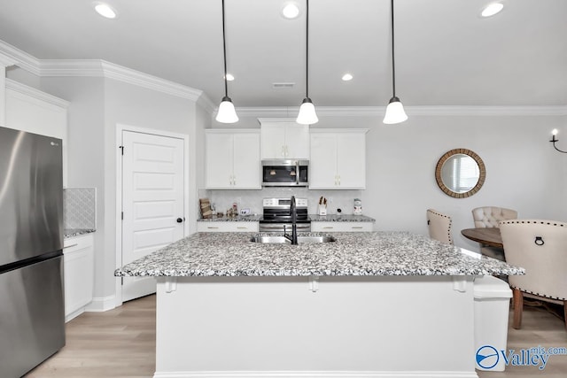 kitchen featuring stainless steel appliances, sink, pendant lighting, white cabinets, and an island with sink