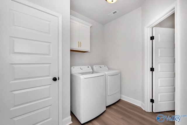 clothes washing area with washer and clothes dryer, cabinets, and wood-type flooring