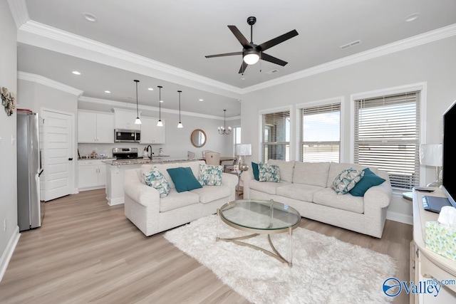 living room featuring ceiling fan with notable chandelier, light hardwood / wood-style flooring, crown molding, and sink