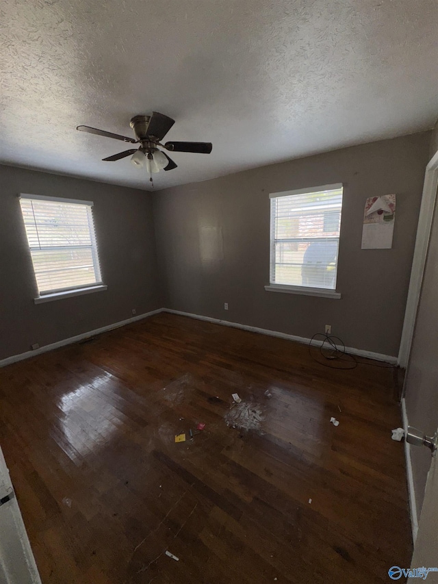 unfurnished room with ceiling fan, dark wood-type flooring, a textured ceiling, and plenty of natural light