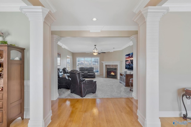 living area featuring a ceiling fan, decorative columns, a fireplace, and ornamental molding