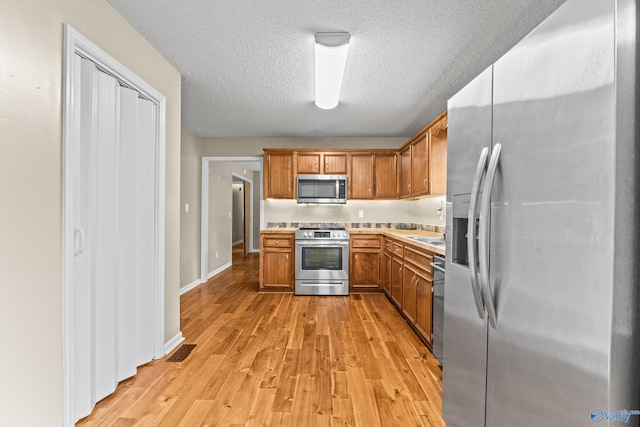 2009 SW Danbury Cir SW, Huntsville, AL 35803 - kitchen with stainless steel appliances, light countertops, brown cabinets, light wood-style floors, and a textured ceiling