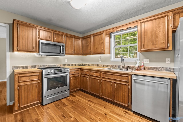 2009 SW Danbury Cir SW, Huntsville, AL 35803 - kitchen with stainless steel appliances, a sink, light wood-type flooring, brown cabinets, and a textured ceiling