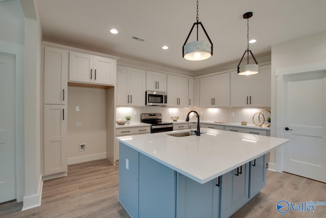 kitchen with a kitchen island with sink, tasteful backsplash, stainless steel appliances, and light hardwood / wood-style floors