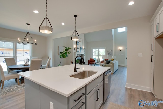 kitchen featuring hanging light fixtures, sink, light hardwood / wood-style flooring, and a center island with sink