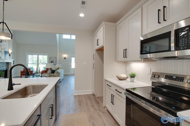 kitchen featuring white cabinetry, light wood-type flooring, appliances with stainless steel finishes, decorative light fixtures, and sink