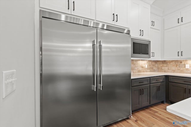kitchen with white cabinetry, built in appliances, light wood-type flooring, and decorative backsplash