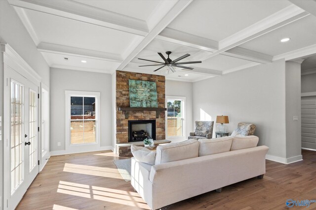 living room featuring hardwood / wood-style flooring, coffered ceiling, a stone fireplace, and beam ceiling