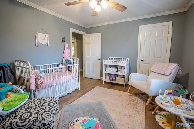 bedroom with crown molding, a textured ceiling, ceiling fan, hardwood / wood-style floors, and a crib