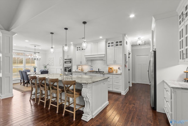 kitchen featuring a breakfast bar, appliances with stainless steel finishes, white cabinets, a center island with sink, and decorative light fixtures