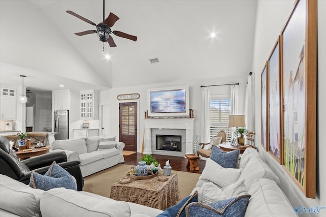 living room with hardwood / wood-style flooring, ceiling fan, and high vaulted ceiling