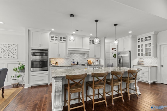 kitchen with appliances with stainless steel finishes, light stone countertops, an island with sink, white cabinets, and a kitchen bar