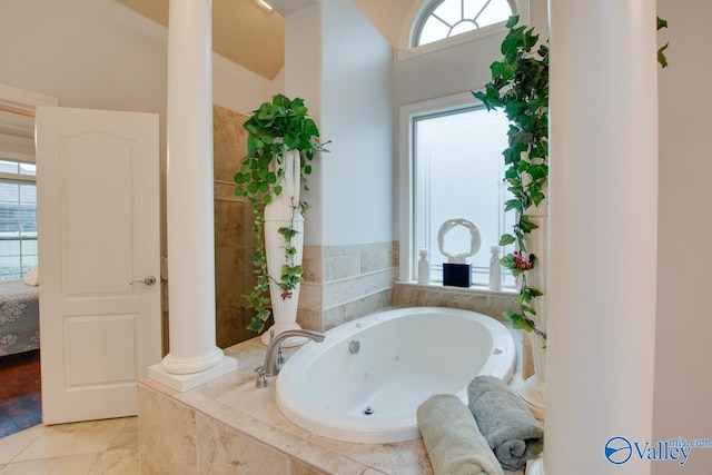 bathroom with tile patterned floors, a healthy amount of sunlight, ornate columns, and tiled tub