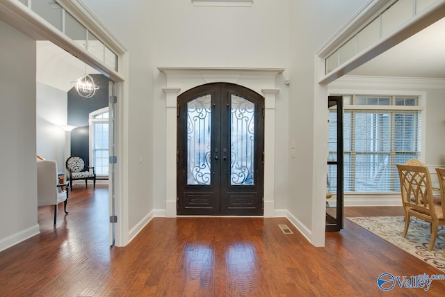 foyer entrance featuring dark hardwood / wood-style floors, ornamental molding, a chandelier, and french doors