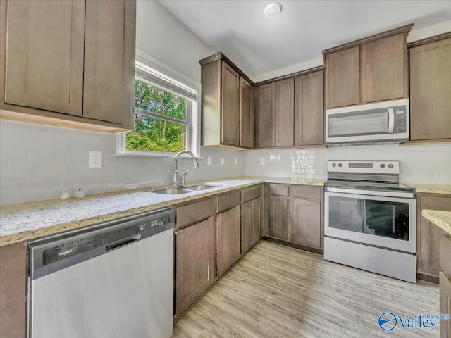 kitchen with stainless steel appliances, a sink, light stone countertops, light wood-style flooring, and tasteful backsplash
