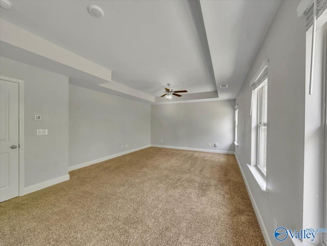 carpeted empty room featuring a ceiling fan, baseboards, and a raised ceiling