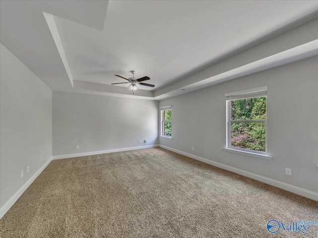 carpeted empty room with a raised ceiling, a ceiling fan, and baseboards