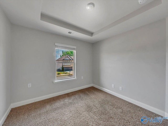 carpeted empty room with a tray ceiling, visible vents, and baseboards