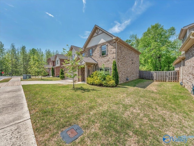 view of side of home with brick siding, a lawn, concrete driveway, and fence