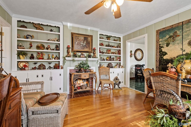 living area featuring built in shelves, ceiling fan, light hardwood / wood-style flooring, crown molding, and a textured ceiling