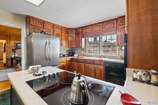 kitchen with a textured ceiling, black electric stovetop, sink, and stainless steel refrigerator