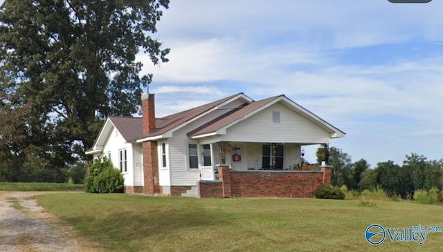 view of front of home with a porch, a chimney, and a front lawn