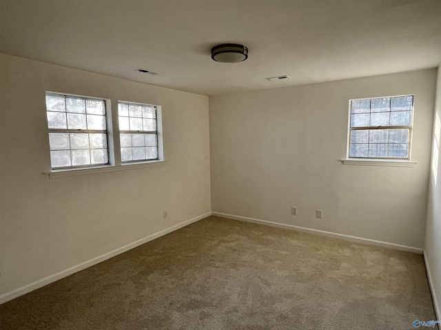 spare room with a healthy amount of sunlight, baseboards, visible vents, and carpet flooring