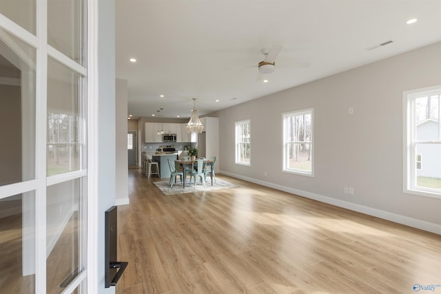 unfurnished dining area featuring ceiling fan with notable chandelier, light hardwood / wood-style flooring, and a wealth of natural light