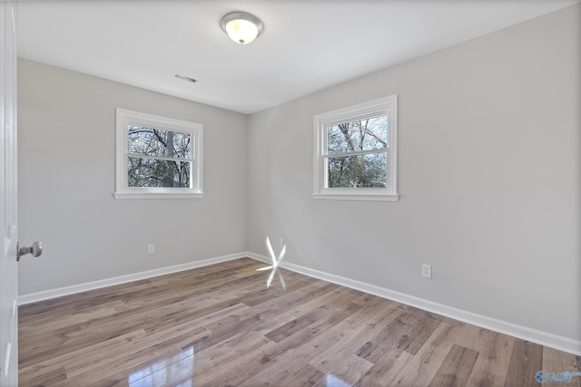 unfurnished room featuring light wood finished floors, visible vents, and baseboards