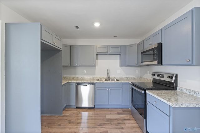 kitchen featuring light wood-type flooring, appliances with stainless steel finishes, light countertops, and a sink