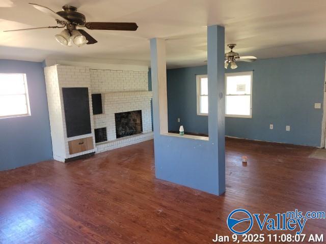 unfurnished living room featuring ceiling fan, a healthy amount of sunlight, dark hardwood / wood-style flooring, and a brick fireplace