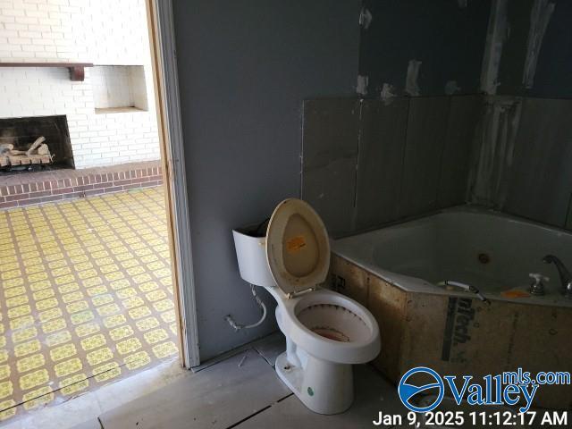 bathroom with a brick fireplace, toilet, and a bathing tub