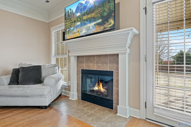 living area with visible vents, baseboards, a tiled fireplace, wood finished floors, and crown molding