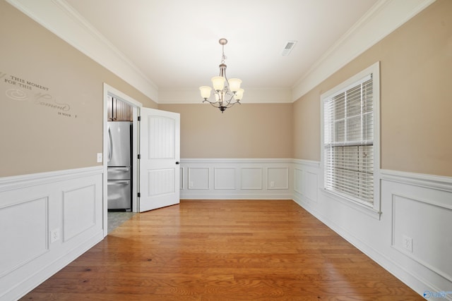 unfurnished dining area with crown molding, light wood finished floors, wainscoting, and an inviting chandelier